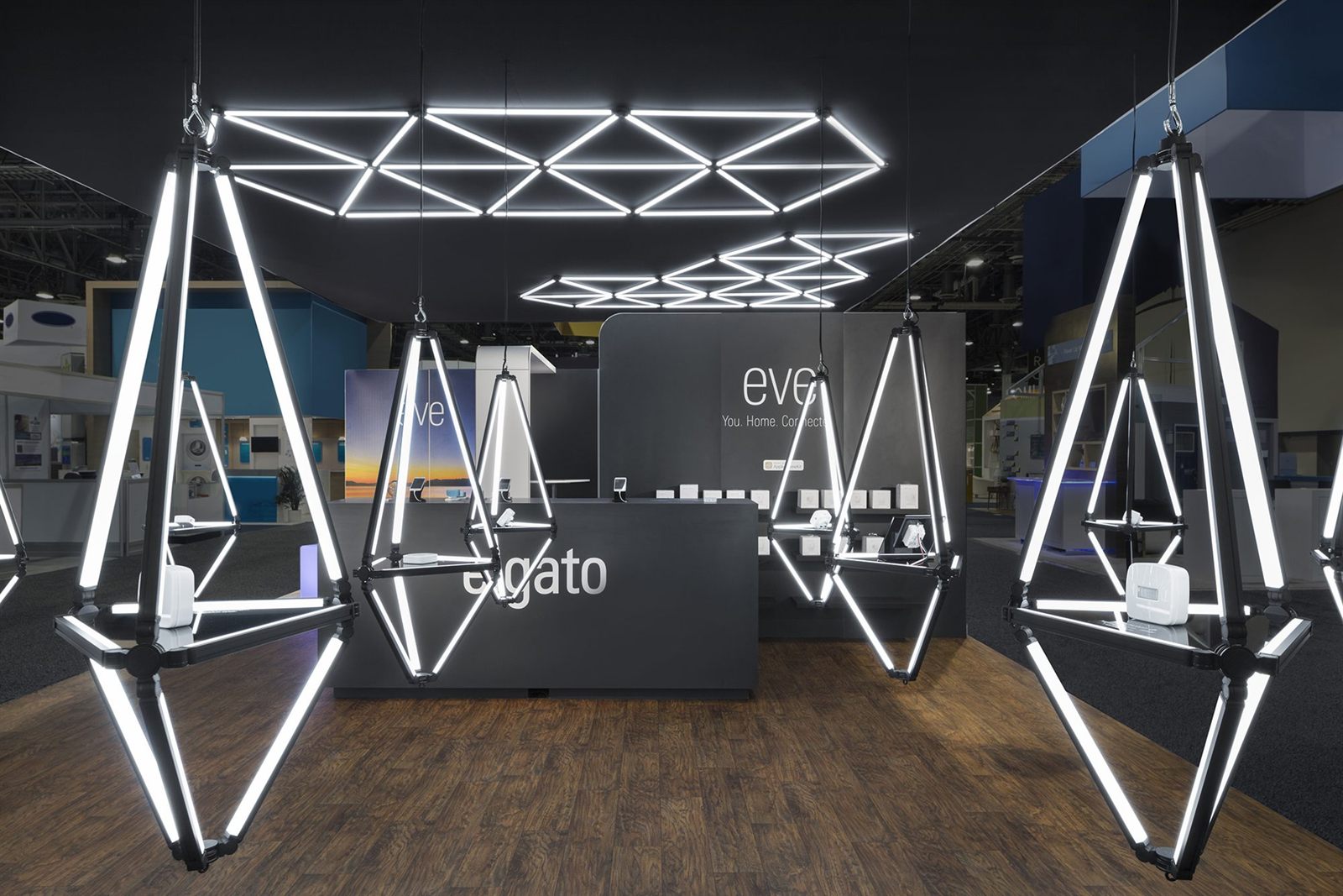 A dark exhibition stand lit by dramatic suspended geometric light fixtures