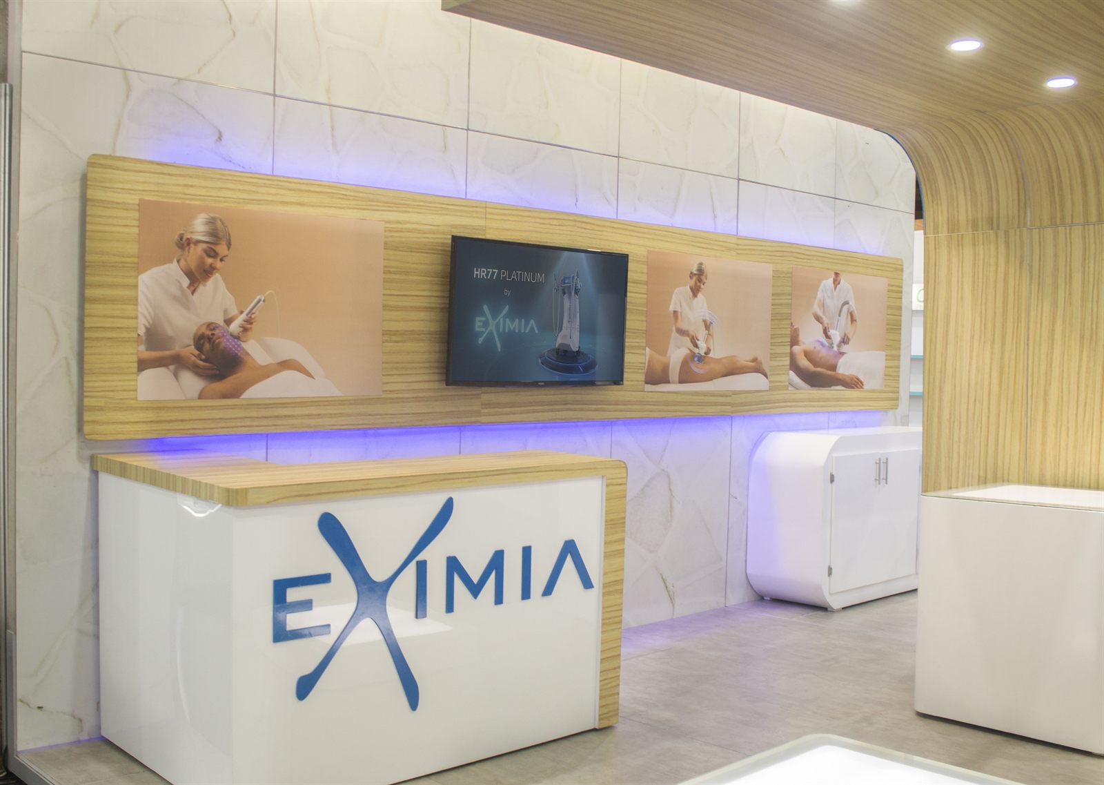 Eximia clinical-premium aesthetics stand by Visualex — backlit treatment imagery and a clean reception desk